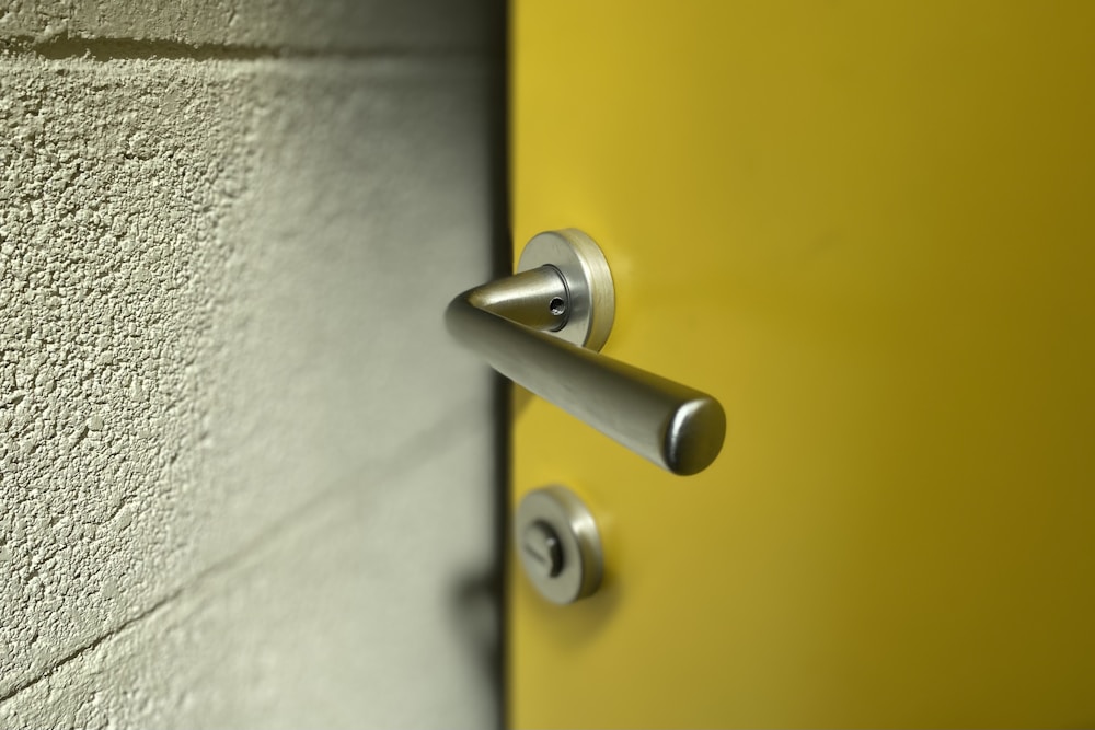 A brushed steel lever handle and lock cylinder on a yellow commercial door
