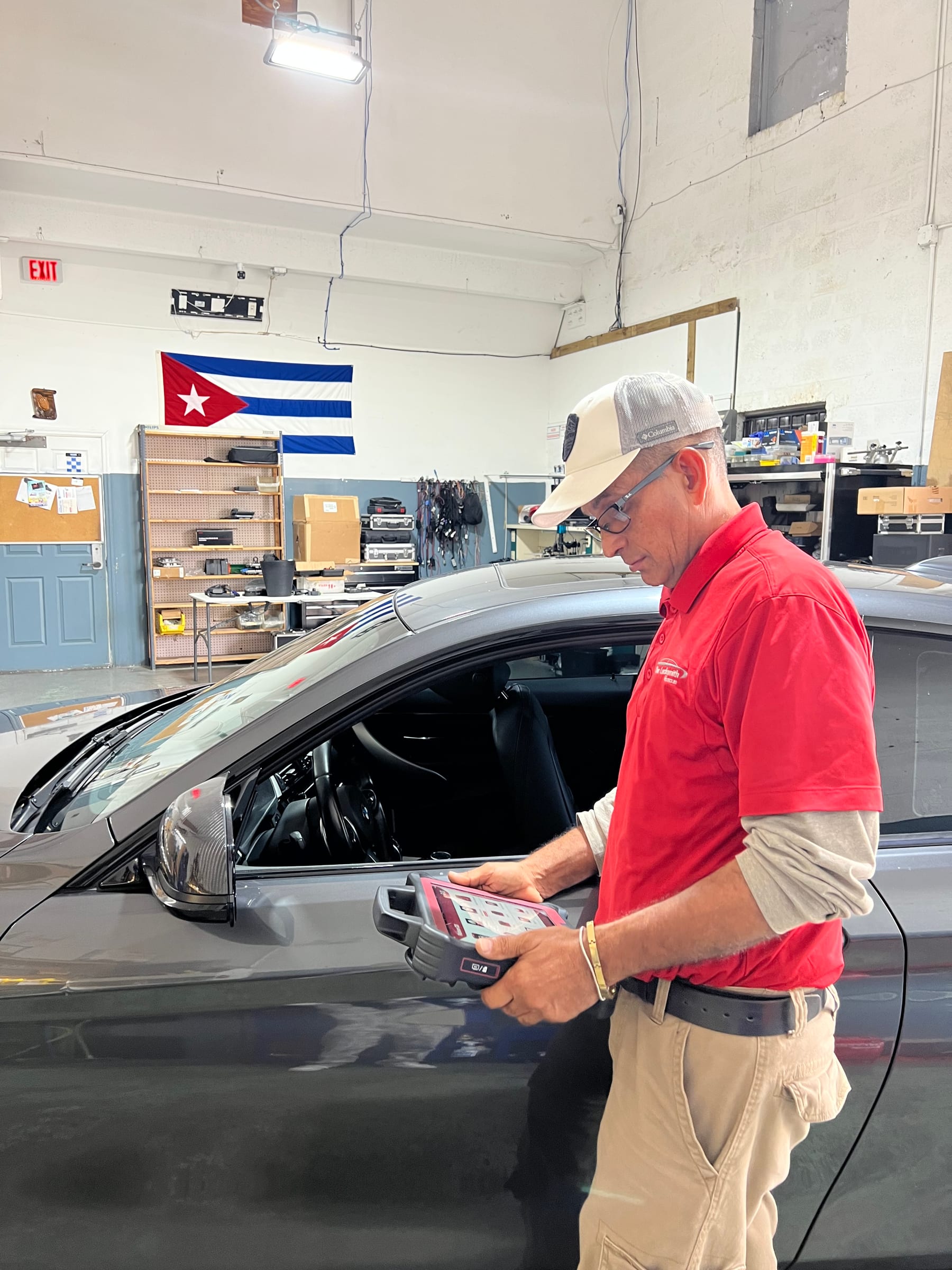 Eddy in his red company polo and cap, standing beside a car in the shop reading a diagnostic tablet