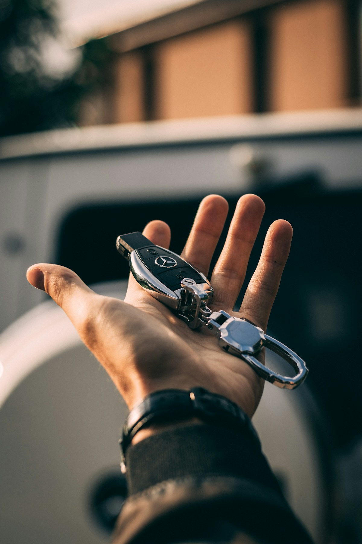 A hand holding a Mercedes smart key and keyring in front of a white van